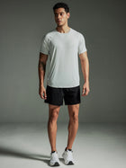 Man wearing a TECHTEE light gray t-shirt and black shorts against a gray background