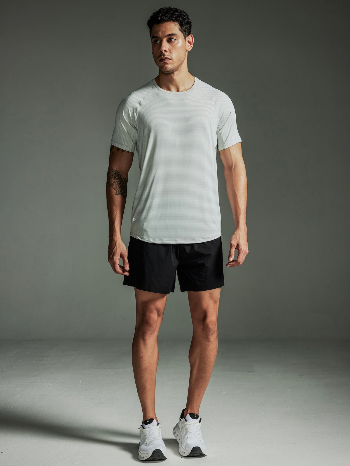 Man wearing a TECHTEE light gray t-shirt and black shorts against a gray background