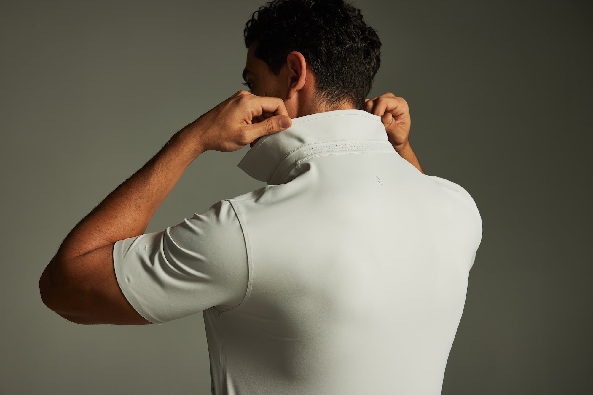 Man adjusting the techtee grey polo shirt against a gray background