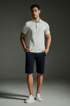 Man wearing the TECHTEE light grey polo shirt and navy shorts against a dark background