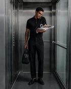 Man in an all black outfit holding a bag and files in an elevator
